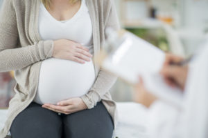 Pregnant woman holding her stomach while sitting in her doctor’s office awaiting results about a possible birth injury